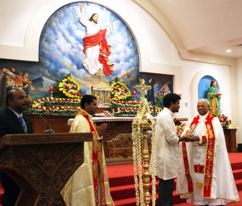 40.	Bishop Jacob Angadiath congratulates Dr. Ginto Pottackal of Baltimore, who painted the striking apse mural of the Ascension. The mural, which frames a statue of Christ ascending to heaven, depicts the scene from Acts 1:6-11.
