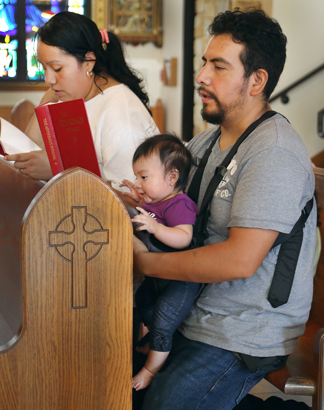 Fidel and Guadalupe Alonzo, with their baby Fatima, pray after the Benediction service at the conclu-sion of the procession.