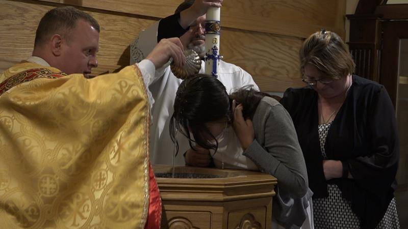 Father Casey Coleman administers the sacrament of baptism to Summer Wilson during the Easter Vigil at St. Mary Mother of God Church in Sylva. (Photo by Joe Holt)