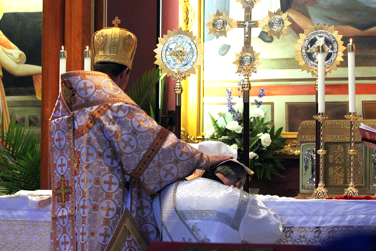 Father Kevin kneels before the altar, resting his forehead on the altar, as Bishop Bohdan lays hands on his head with the symbol of his episcopal authority, the omophorion, and making the sign of the cross over his head three times.
