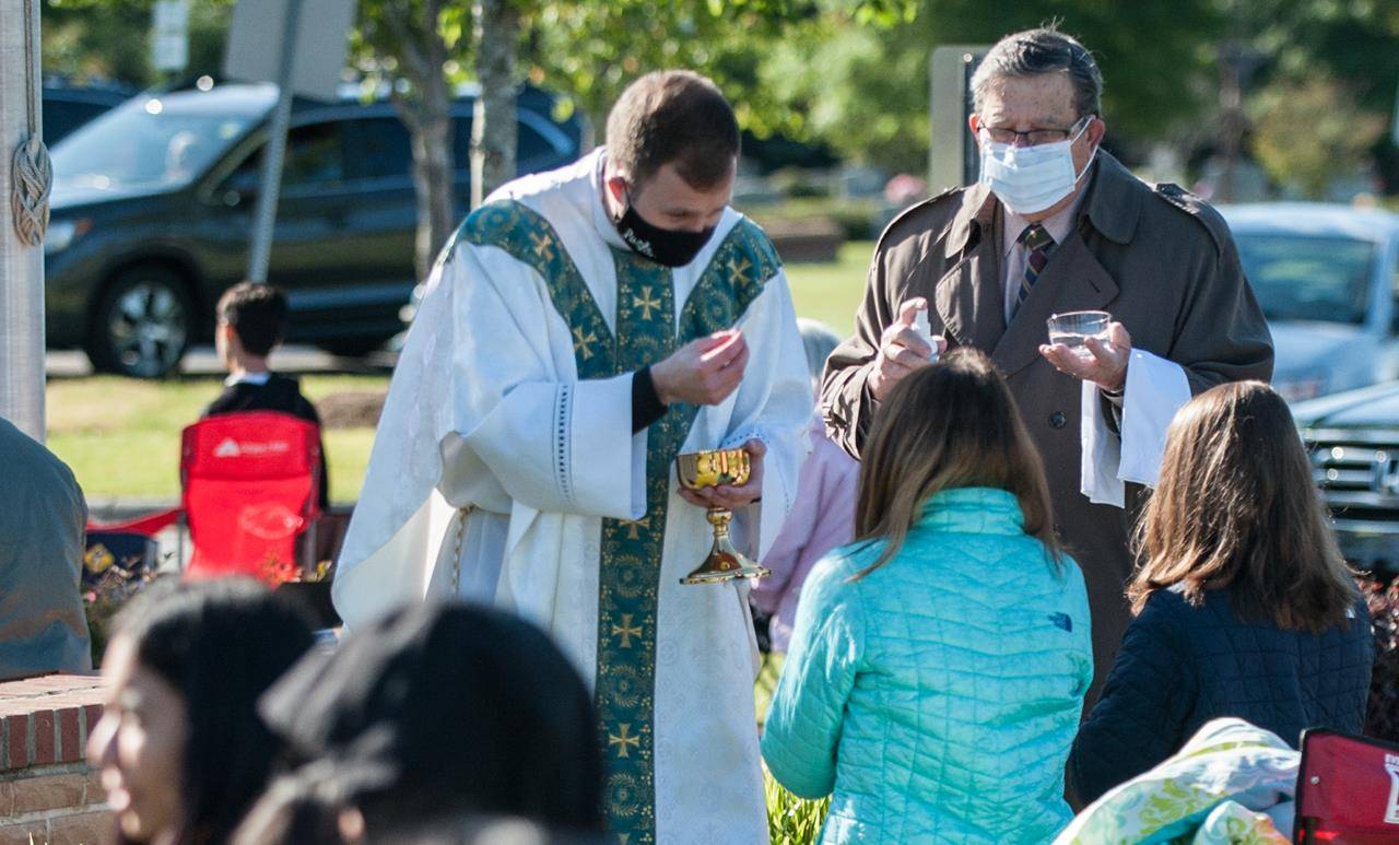 Father John Eckert, pastor of Sacred Heart Church in Salisbury, distributes Holy Communion at the parish’s outdoor Mass May 17. (Bill Washington | Catholic News Herald)